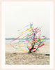 An image of a tree on a riverbank, surrounded by colourful ribbons blowing in the breeze, by Polish artist Oliver Schwarzwald. The image is presented in a white wooden frame. 