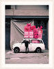 An image of a Mini car with pink presents piled on top, by Polish artist Oliver Schwarzwald, in a white frame. 