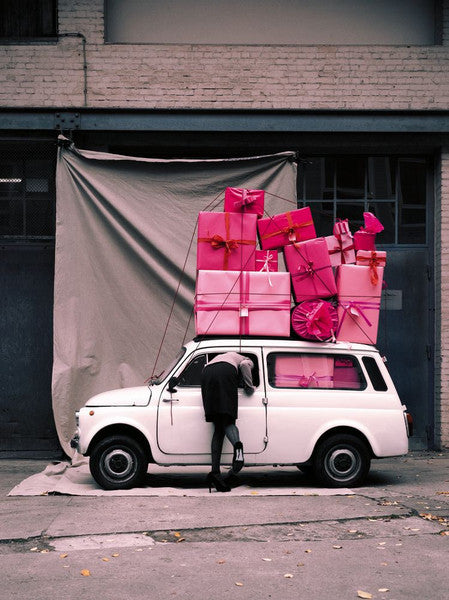 A image of a Mini car with pink presents piled on top and a woman leaning inside, by Polish artist Oliver Schwarzwald.